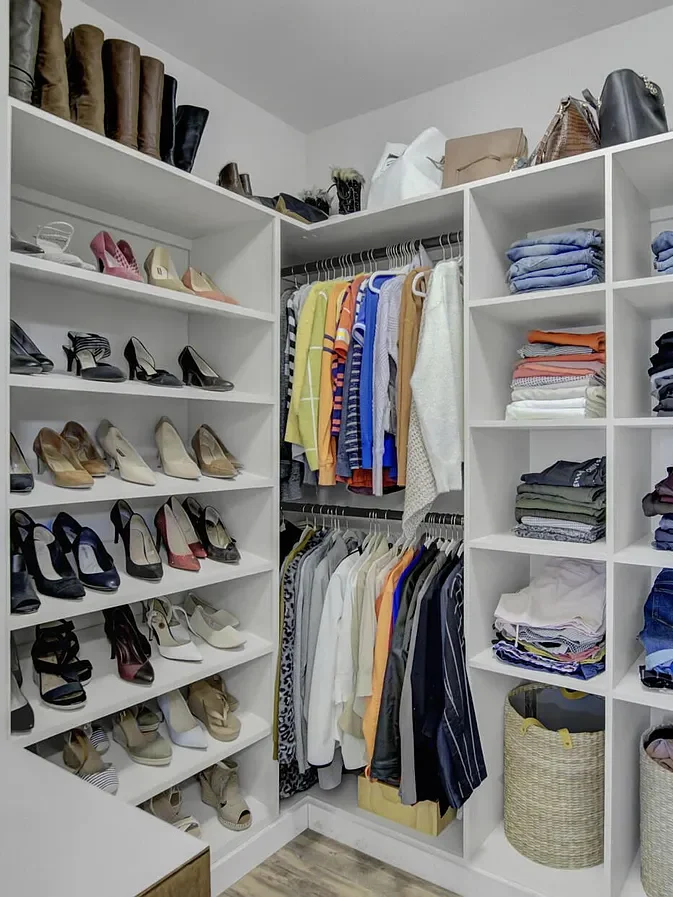 Custom walk-in closet with white built-in storage, organized shoe shelving, hanging sections, and folded clothing compartments.