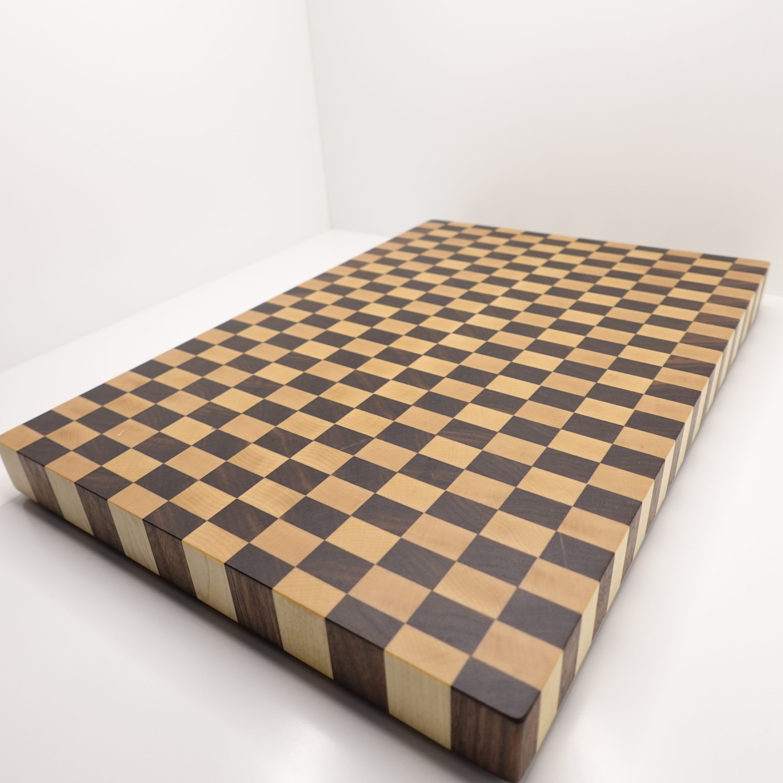 Handmade walnut and maple checkered end grain cutting board with a geometric pattern.